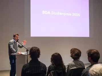 Prof. Andreas Fuchs steht vor dem Publikum und begrüßt die Gäste des BDA Studienpreises.