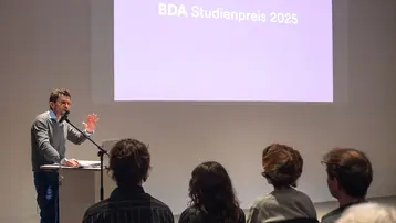 Professor Andreas Fuchs stands in front of the audience and welcomes the guests to the BDA Study Prize ceremony.