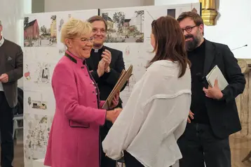 Böttiger Prize 2025, Marie-Luise Stoll-Steffan (Wiesbaden Foundation) and Prof. Daniel Seiberts (HSRM) congratulate the prize winner Nicoletta Leindl. Plans of her architectural design can be seen in the background.
