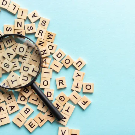 Blauer Hintergrund, verschiedenen Bausteine mit Buchstaben, obendrüber eine Lupe