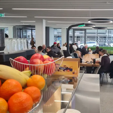 eine Theke mit Obst, Kaffee und Studentenfutter, im Hintergrund Studierende an Tischen