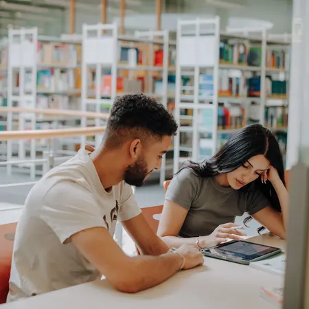 Zwei Studierende sitzen an einem Tisch und arbeiten