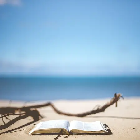 Ein aufgeschlagenes Buch liegt am Strand. Man kann das Meer im Hintergrund sehen