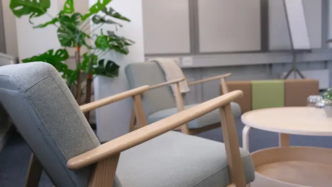 Ein modern eingerichteter Raum mit zwei hellblauen Sessel aus Holz, einem runden Tisch in der Mitte und einer großen, grünen Pflanze im Hintergrund. Der Raum vermittelt eine einladende und entspannte Atmosphäre.