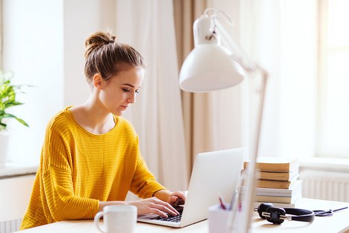 Junge, blonde Frau arbeitet an einen Schreibtisch sitzend an ihrem Laptop 