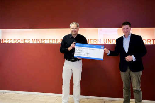 Staatssekretär Dr. Stefan Heck überreicht Prof. Dr. Steffen Reith von der Hochschule RheinMain eine Förderzusage in Höhe von 350.000 Euro für das Projekt PROGENITOR.