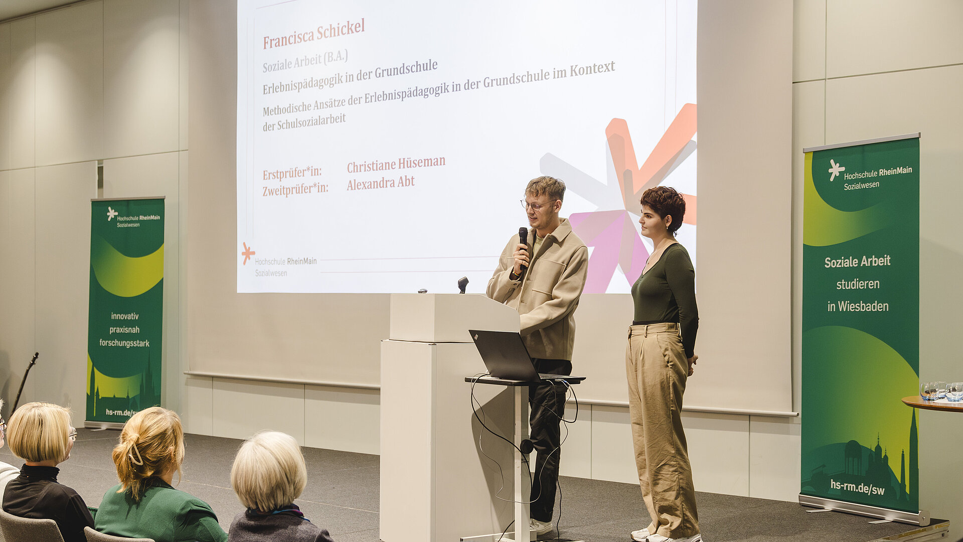zwei Menschen stehen auf der Bühne und halten eine Rede 