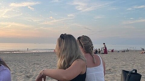 Mehrere Personen sitzen auf Decken am Strand. Das Meer ist im Hintergrund