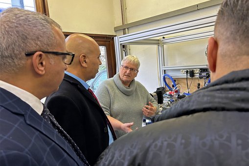 Prof. Dr. Birgit Scheppat steht vor einem Versuchsaufbau im Labor für Wasserstofftechnologie und Energiespeicher und erläutert der marokkanischen Delegation die Hintergründe eines Forschungsprojekts