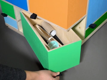 A hand is pulling open a green drawer from a multicolored storage unit. Inside the drawer are various tools, including a brush, a roll of tape, and a small device. The overall composition emphasizes organizational efficiency in a colorful design.