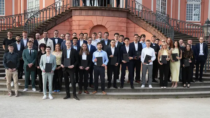 Die Absolvent:innen der Informatik an der HSRM stehen für ein Gruppenfoto mit ihren Urkunden vor dem Schloss Biebrich.