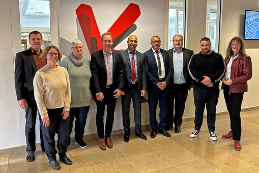 Prof. Dr. Bernhard Gross, Judith Hayer, Prof. Dr. Birgit Scheppat, Prof. Dr. Christian Glockner, Prof. Hassan Mharzi, Mostafa El Gameh, Prof. Dr. Andreas Brensing, Karim Bouazzi und Prof. Dr. Ulrike Stadtmüller stehen für ein Gruppenfoto im Foyer des A-Gebäudes vor dem Key Visual der Hochschule RheinMain