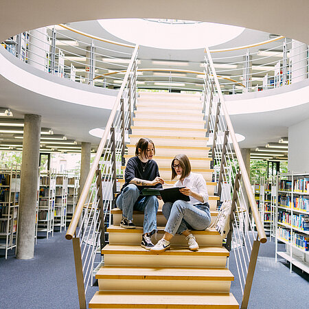 Wiesbaden Business School Bibliothek Studierende sitzen auf einer Treppe in der Bibliothek der Wiesbaden Business School