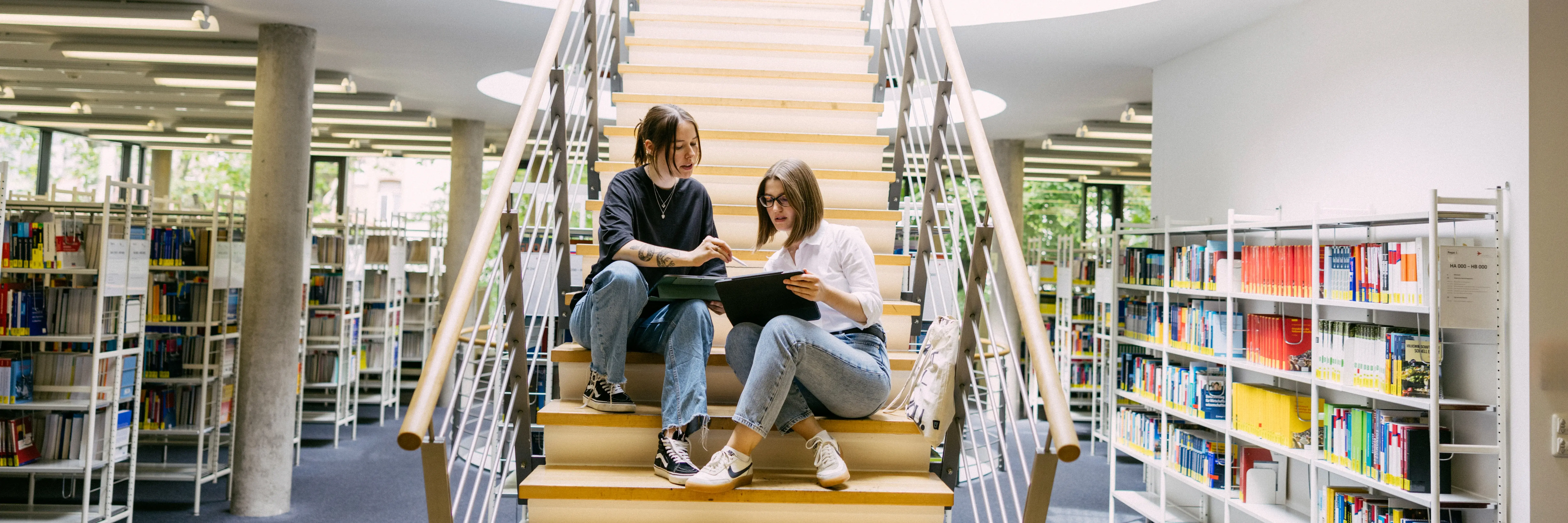 Wiesbaden Business School Bibliothek Studierende sitzen auf einer Treppe in der Bibliothek der Wiesbaden Business School