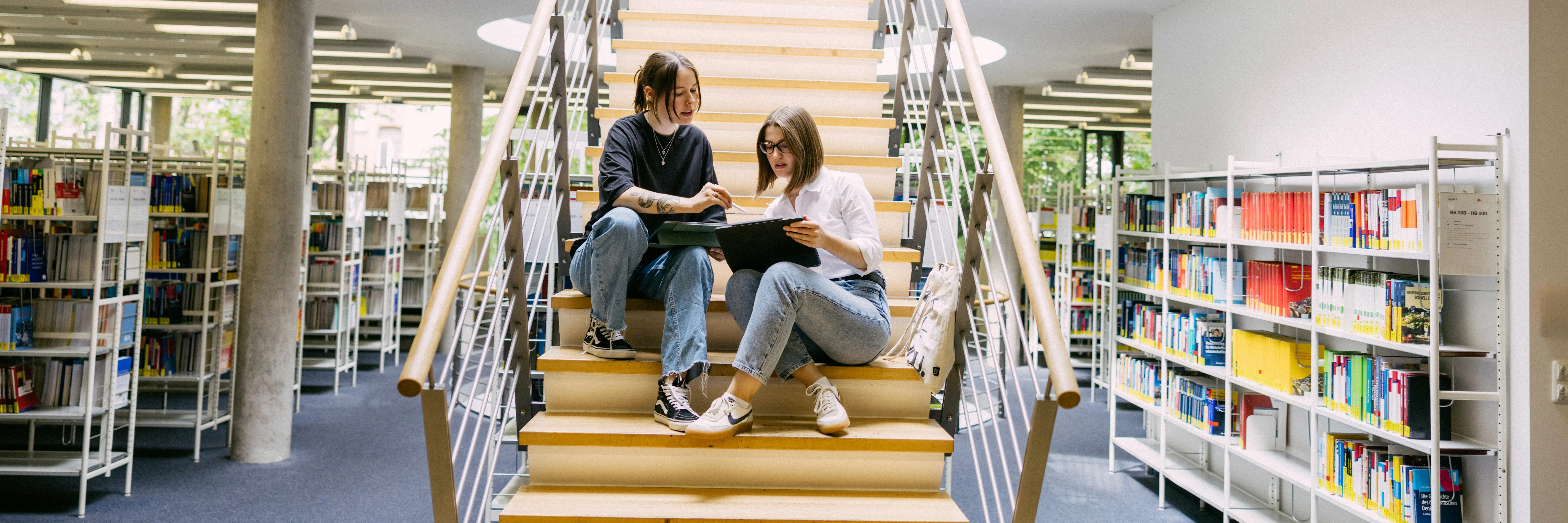 Studierende sitzen auf einer Treppe in der Bibliothek der Wiesbaden Business School