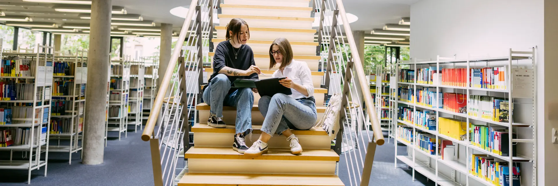 Studierende sitzen auf einer Treppe in der Bibliothek der Wiesbaden Business School