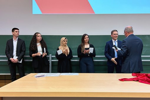 Fünf Absolvent:innen nehmen nacheinander die Glückwünsche eines Professors entgegen.