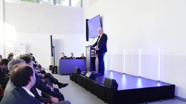 Patrick Burghardt steht auf einer Bühne und spricht zu einem Publikum. 