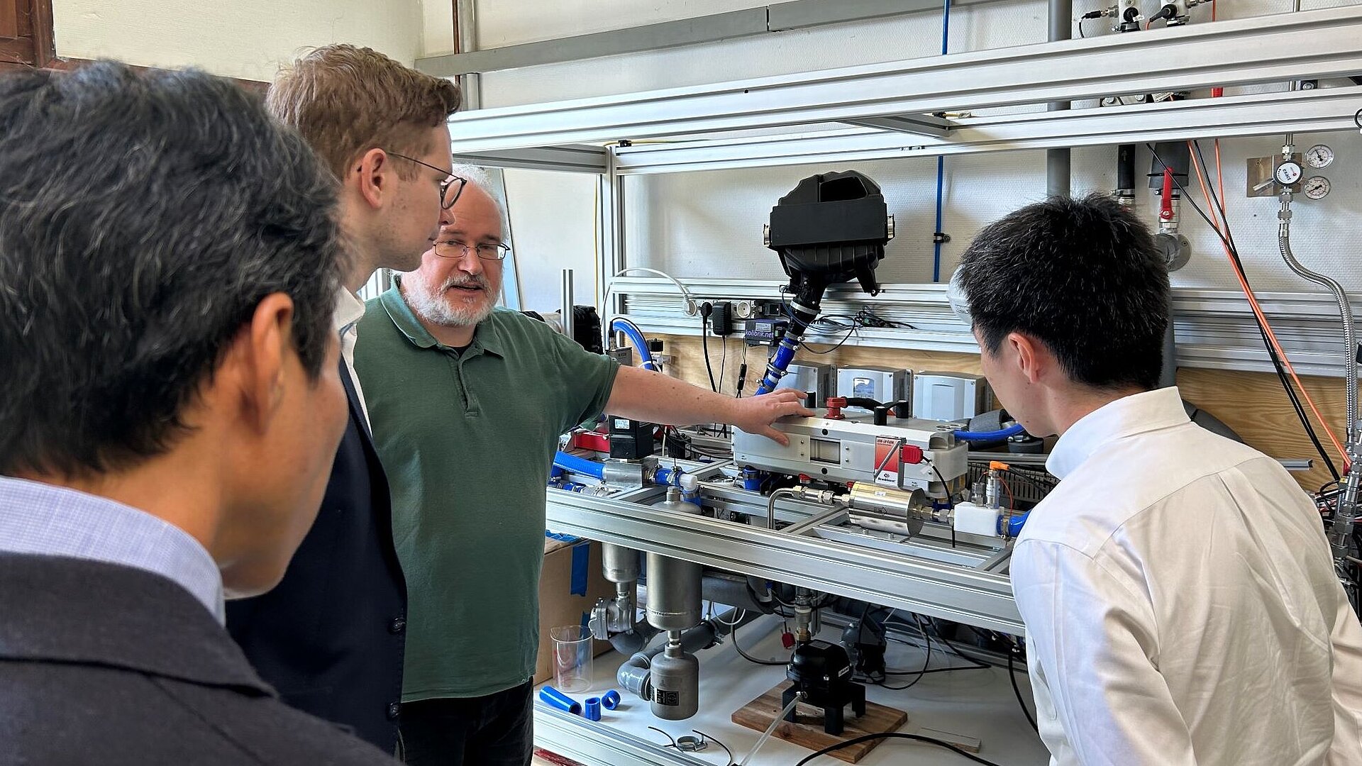Wissenschaftlicher Mitarbeiter Georg Derscheid mit japanischer Delegation im Wasserstofflabor. Georg Derscheid, wissenschaftlicher Mitarbeiter im Wasserstofflabor, führt den Teststand für Brennstoffzellenkomponenten vor