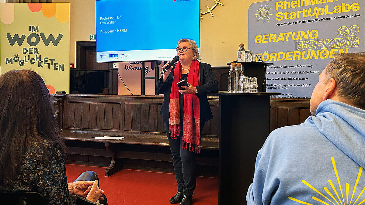 Hochschulpräsidentin Prof. Dr. Eva Waller hält ein Mikrofon in der Hand und spricht ein Grußwort zum Publikum im Heimathafen im Alten Gericht.