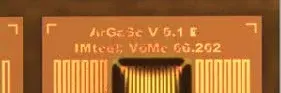 An electronic microchip is depicted, featuring gold-colored circuitry with labeled sections. The text includes "ArGeSe V 5.1 E" and "IMtech V0Me 60.262." The design showcases intricate lines and patterns typical of semiconductor components.