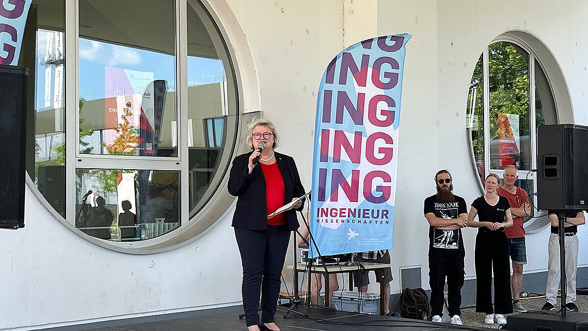 Prof. Dr. Eva Waller steht auf einer Bühne und hält ein Mikrofon in der Hand