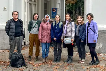 Five students from the Master's programme in Architectural Heritage and their two teachers stand in front of the entrance gate to the University of Antwerp. They are in Antwerp for the international HERILAND programme.