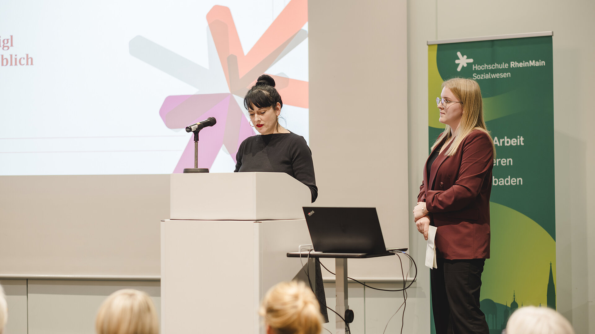 zwei Frauen stehen auf der Bühne und halten eine Rede 