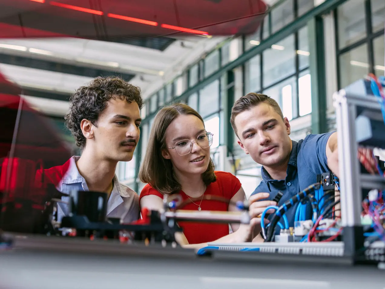Zwei Studenten und eine Studentin betrachten sich einen Versuchsaufbau