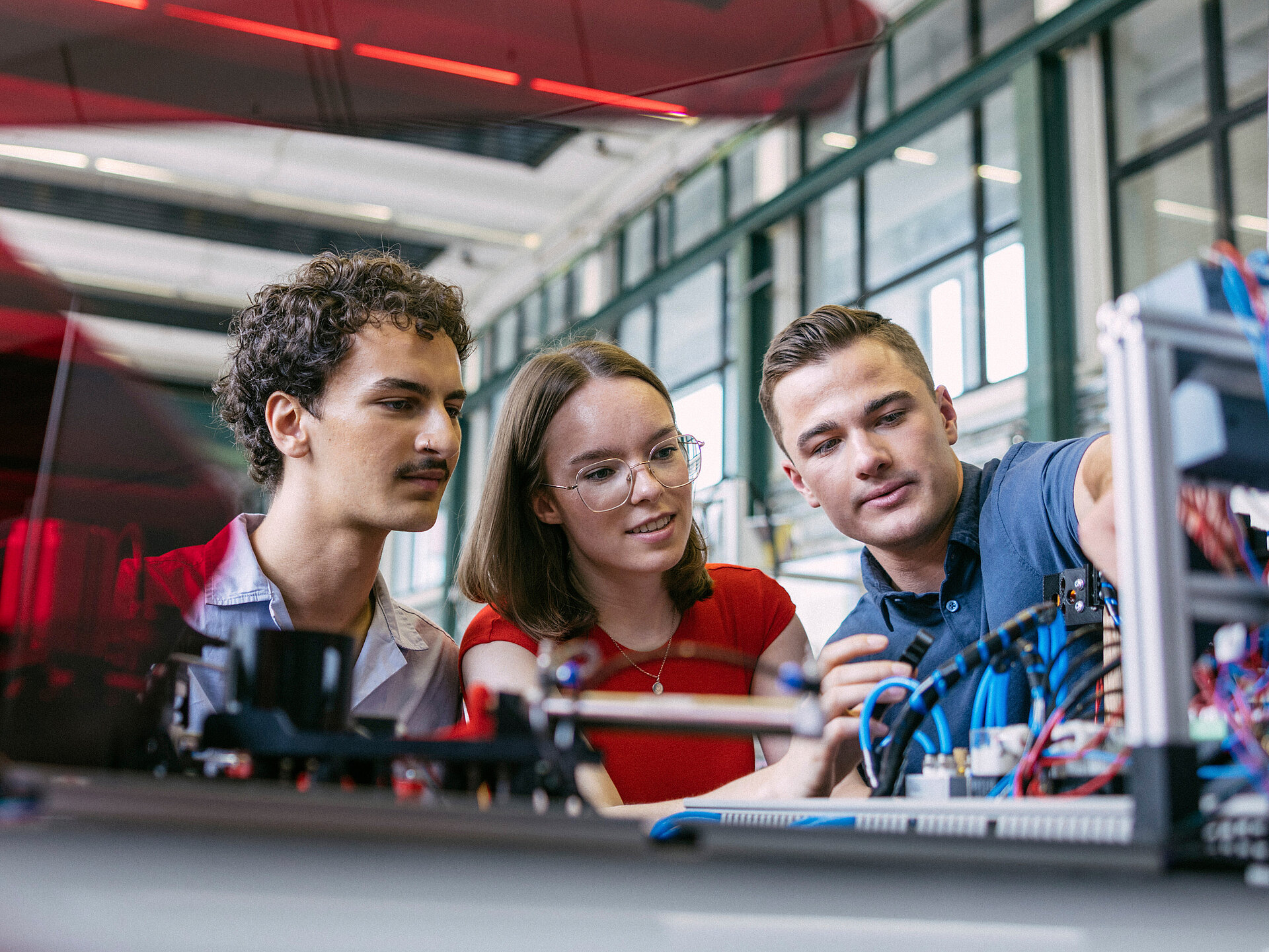 Zwei Studenten und eine Studentin betrachten sich einen Versuchsaufbau