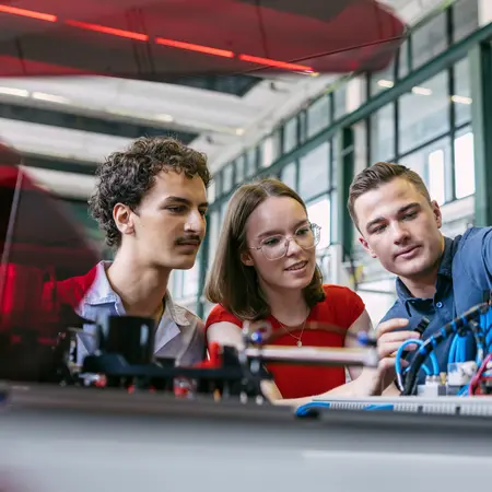 Zwei Studenten und eine Studentin betrachten sich einen Versuchsaufbau