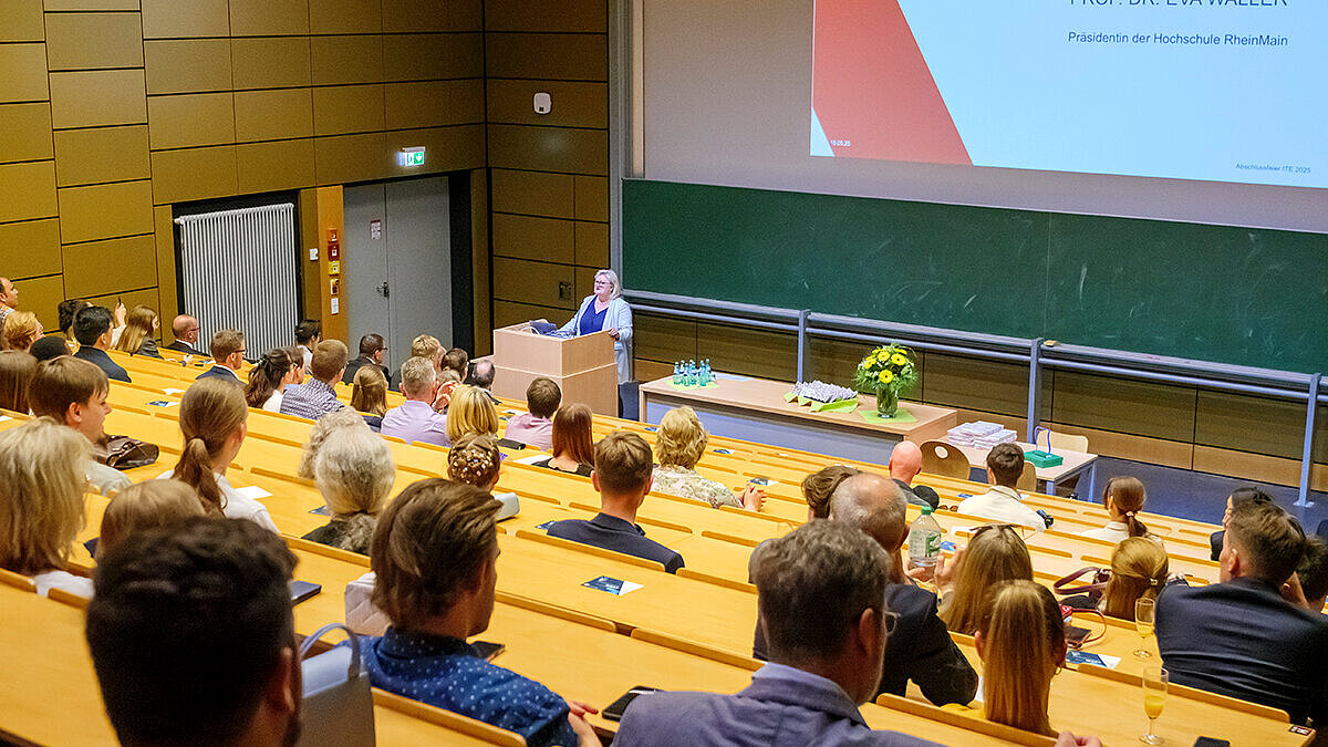Hochschulpräsidentin Prof. Dr. Eva Waller steht am Rednerpult im vollen Hörsaal