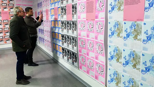 Zwei Personen sehen sich die Motive des Hochschulkalenders 2026 an.