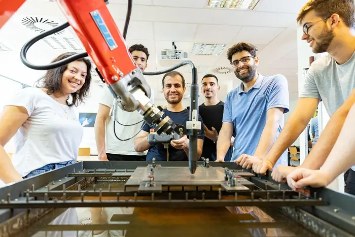 Junge Menschen stehen an einem roten Industrieroboter und schauen in die Kamera.