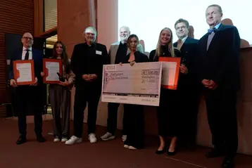 Eine Gruppe von acht Personen steht zusammen auf einer Bühne. Lynn-Bodenheimer, Cheyenne Walz und Irene Schmidt erhielten Preise von Praxispartner Drees & Sommer, die sie in den Händen halten. In der Mitte halten die Personen einen Scheck über 500 Euro für Irene Schmidt. 