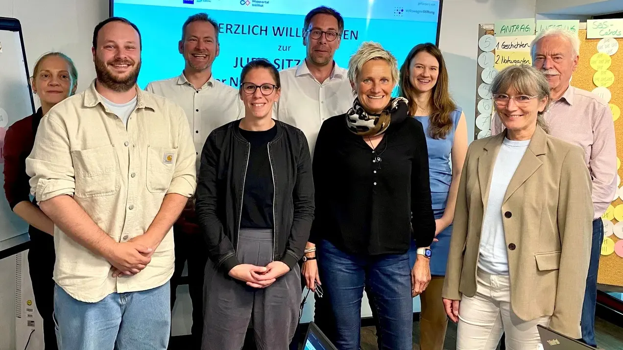 Eine Gruppe von neun Personen steht vor einem Bildschirm, auf dem „Herzlich Willkommen zur Jugendsitzung“ steht. Die Teilnehmer wirken freundlich und engagiert, einige halten Stifte oder Notizen in der Hand. Der Raum ist hell und kreativ gestaltet.