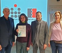 Prof. Rüdiger Pichler steht mit der Gewinnerin Lara Čadež sowie Dr. Klaus Bernsau und Dr. Sandra Steinbrink vom Projekt RheinMain StartUpLabs vor dem Siegerlogo