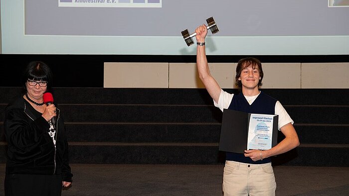 HSRM-Student Moritz Pähler steht während der Preisverleihung des exground filmfest 2024 auf der Bühne und reckt seinen Preis in die Höhe.