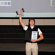 HSRM-Student Moritz Pähler steht während der Preisverleihung des exground filmfest 2024 auf der Bühne und reckt seinen Preis in die Höhe.