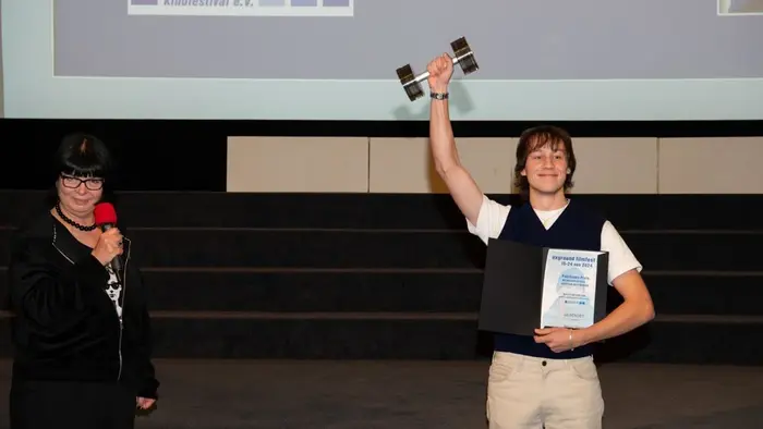 HSRM-Student Moritz Pähler steht während der Preisverleihung des exground filmfest 2024 auf der Bühne und reckt seinen Preis in die Höhe.
