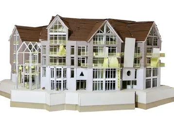A detailed architectural model of a multi-storey residential building with numerous windows and balconies. The façade is light in colour and the roofs are sloping. It is the architectural model ‘House of Generations’ by Liv Ettingshausen.