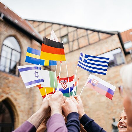 Es sind Hände zu sehen, die verschiedene EU und andere Papierflaggen in die Höhe halten