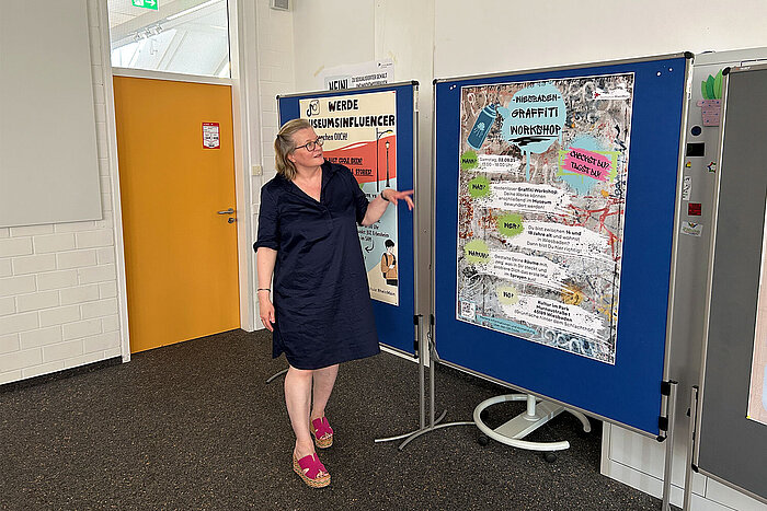 Prof. Dr. Marion Kamphans zeigt auf Plakate, die an Stellwänden angebracht sind.