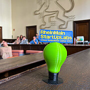 Auf einer Holzbank im Schwurgerichtsaal des Alten Gerichts in Wiesbaden steht der 3-D-gedruckte Pokal des Green Innovation Camps. Im Hintergrund ist an der Wand der hessische Löwe zu sehen.