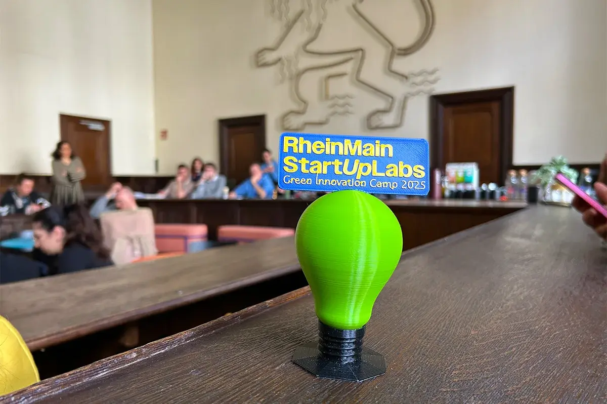 Auf einer Holzbank im Schwurgerichtsaal des Alten Gerichts in Wiesbaden steht der 3-D-gedruckte Pokal des Green Innovation Camps. Im Hintergrund ist an der Wand der hessische Löwe zu sehen.