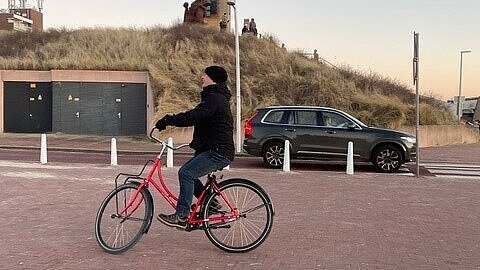 Auf dem Bild sieht man eine Frau, die Fahrrad fährt. Im Hintergrund sind Dünen