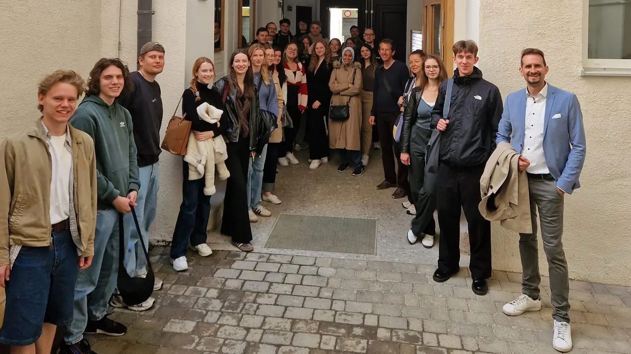 A group of about 30 architectural heritage students are standing in a corridor. They are smiling warmly at the camera. The students are on an excursion in Vienna.