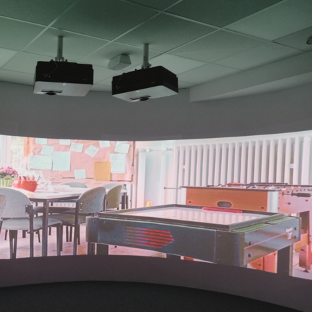Immersionskino Medienkachel Schulzimmer als Hintergrund auf einer gecurvten Leinwand mit zwei Projektoren auf diese gerichtet.