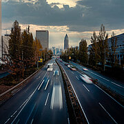 vierspurige Straße mit Hochhäusern und dem Messeturm Frankfurt im Hintergrund