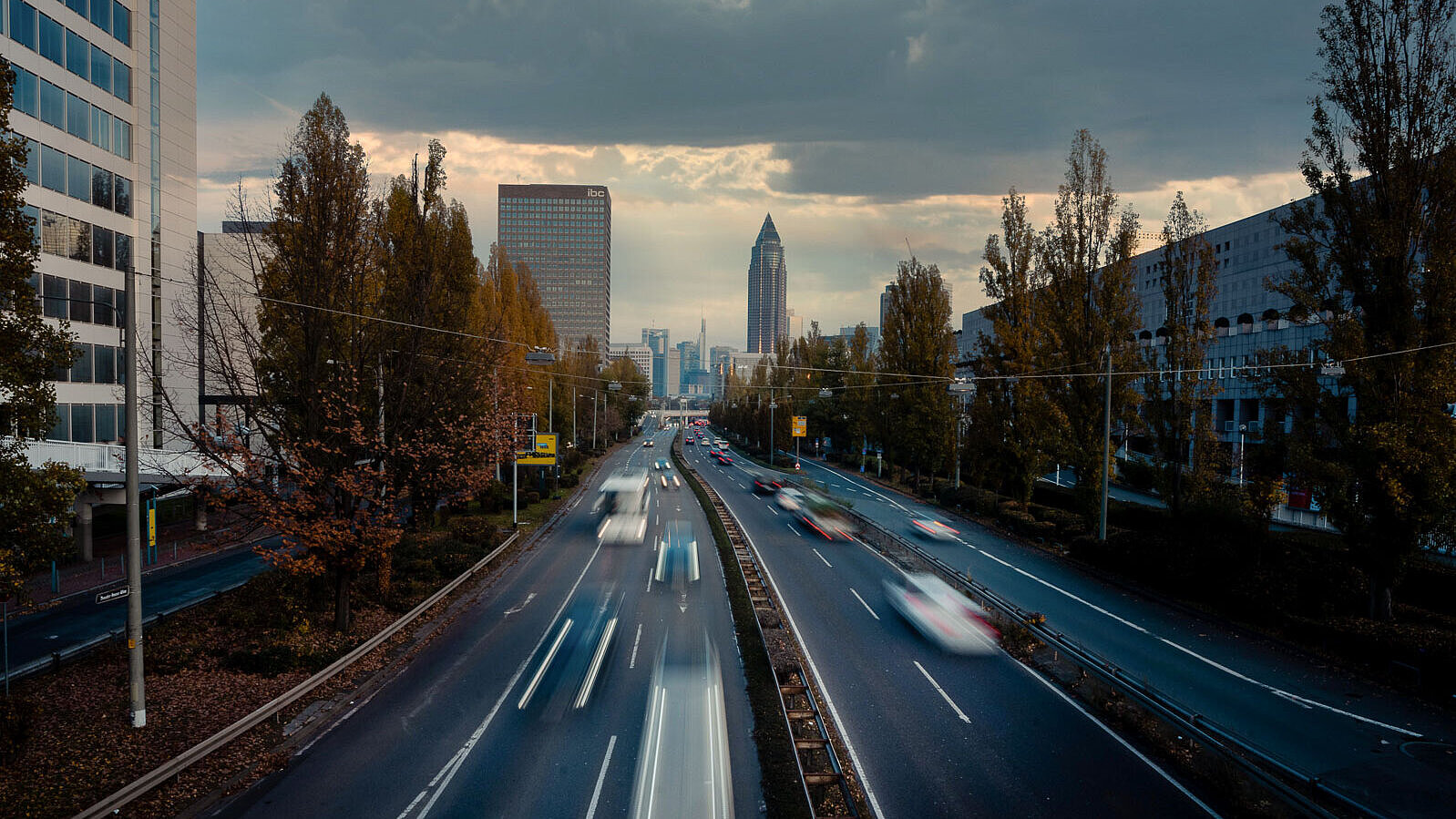 vierspurige Straße mit Hochhäusern und dem Messeturm Frankfurt im Hintergrund
